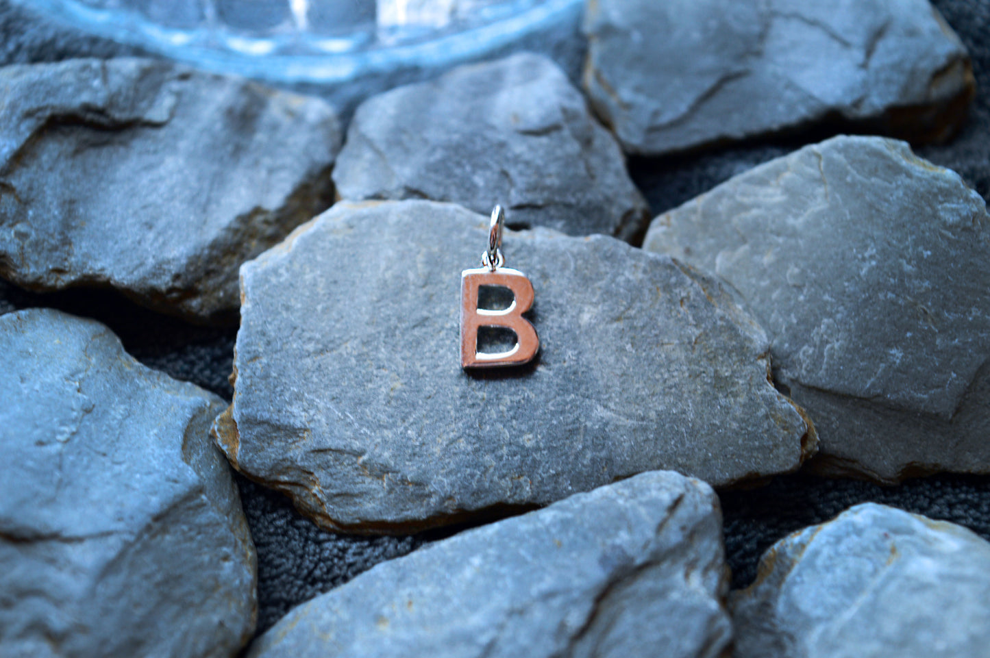 Close-up of a polished sterling silver letter pendant, 10mm tall and 8mm wide, with a 3.5mm loop for necklace chains.