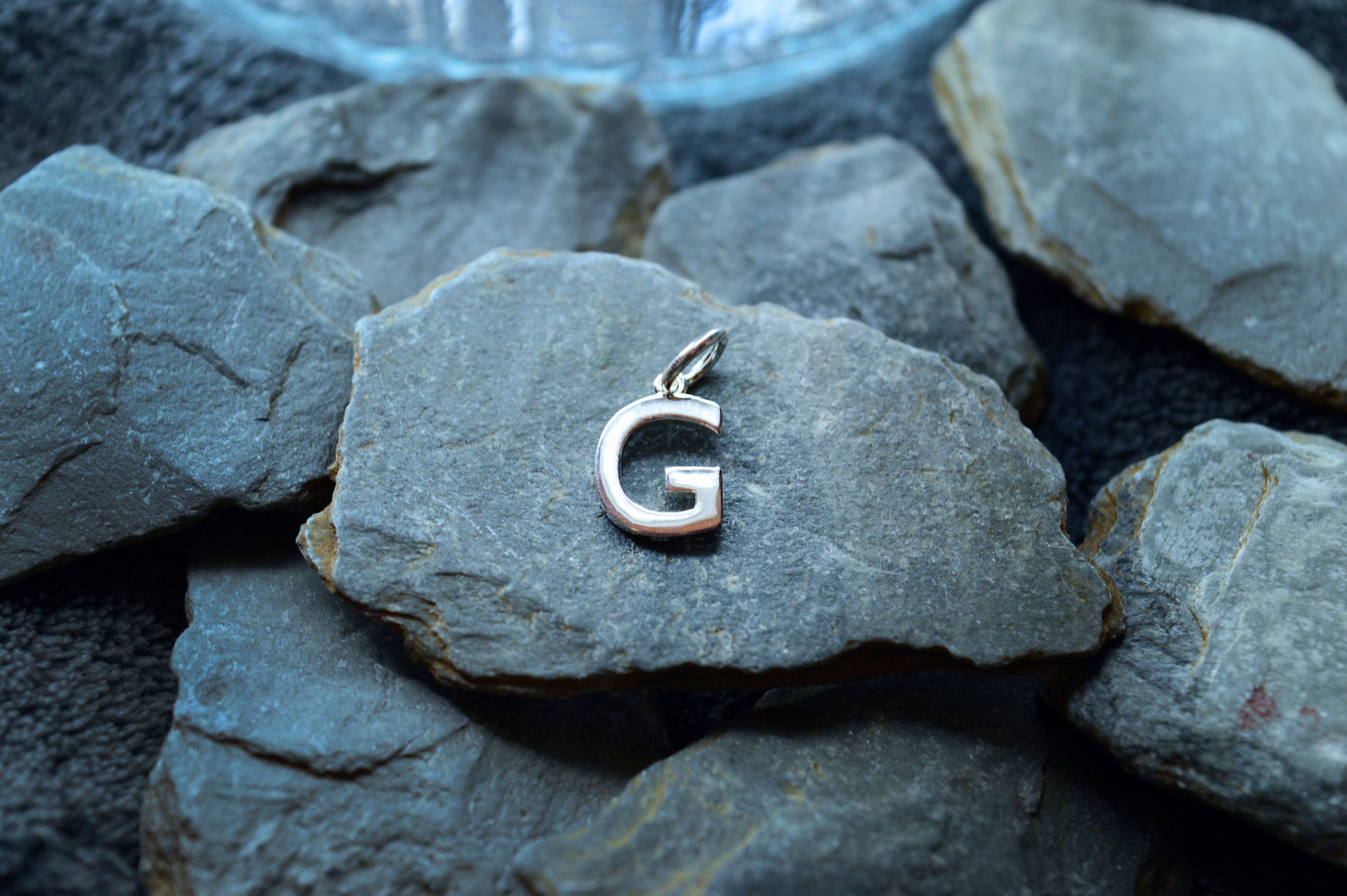 A small, dainty sterling silver letter pendant with a polished finish, measuring 10mm high and 8mm wide.